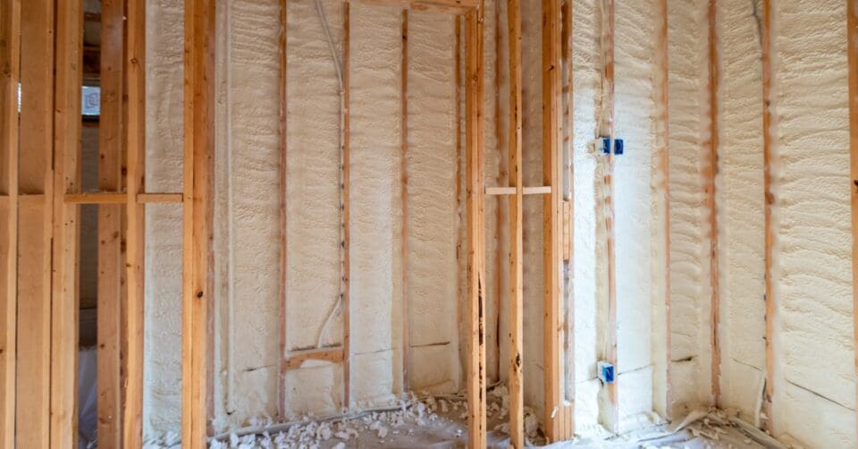 The home's wooden wall frames are filled with spray foam insulation. The floors are covered in a white protective sheet.